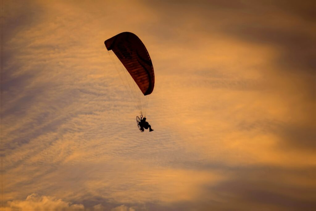 Paraglider soaring against a dramatic sunset sky
