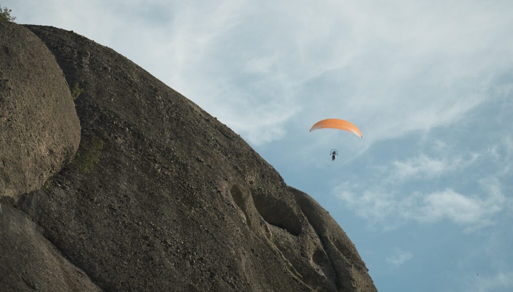 Paraglider flying over a rocky cliff