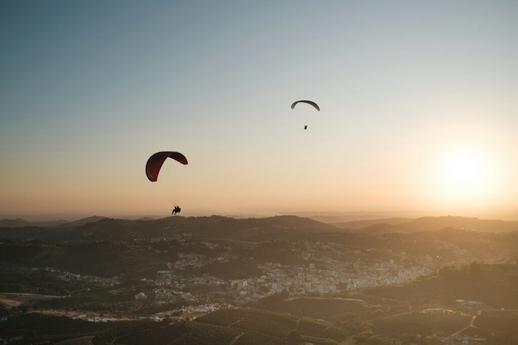 Two paragliders soaring at golden hour above hills